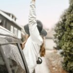 Carefree woman enjoying a rainy road trip, hand outstretched from car window.